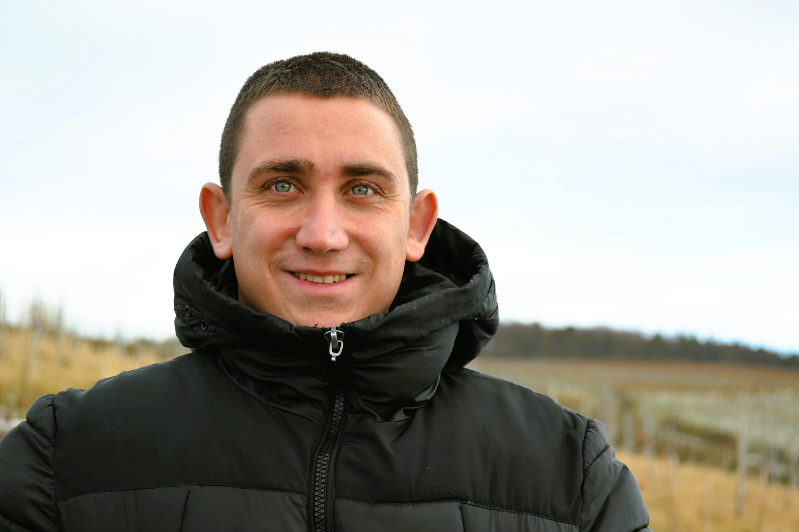 A man smiling warmly in a black winter coat, standing outdoors in Weinstadt, Germany.